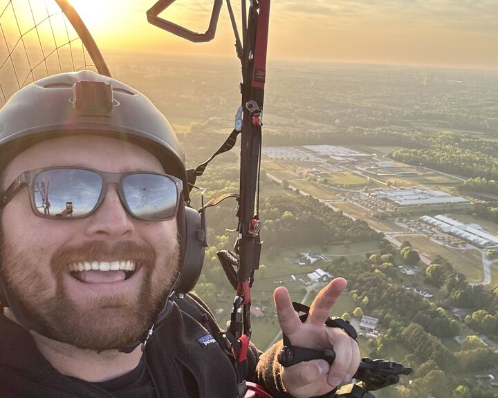 Alex Lang smiling mid-flight on his paramotor at sunrise